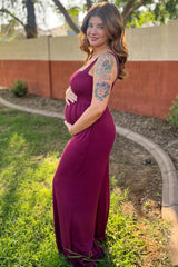 woman wearing a burgundy maternity maxi dress and holding her baby bump in a garden setting