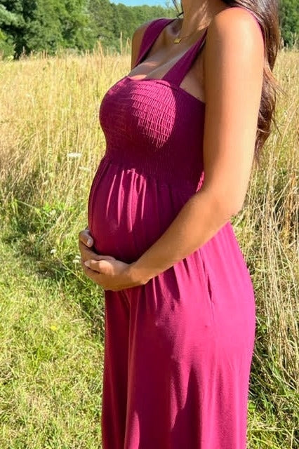 pregnant woman in a magenta smocked maternity dress holding her belly in a grassy field