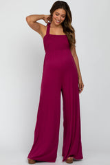 woman wearing a fuchsia maternity jumpsuit with a smocked bodice and wide leg style, showing her baby bump