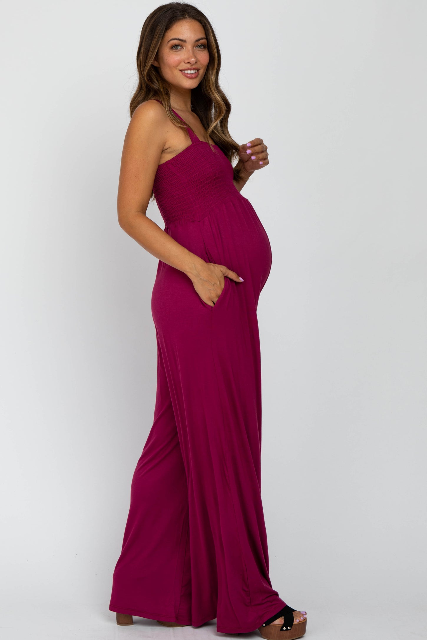 woman wearing a fuchsia strapless maternity jumpsuit with side pockets and a visible baby bump