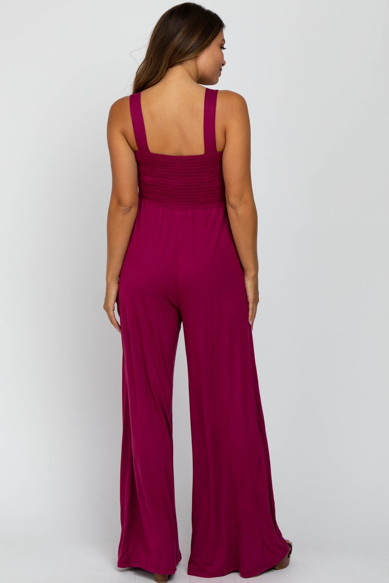 woman wearing a back view of a fuchsia maternity jumpsuit with a smocked bodice and wide leg pants