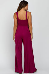 woman wearing a back view of a fuchsia maternity jumpsuit with a smocked bodice and wide leg pants