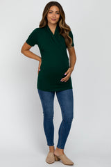 woman wearing a dark green short sleeve maternity top and holding her baby bump with blue skinny jeans