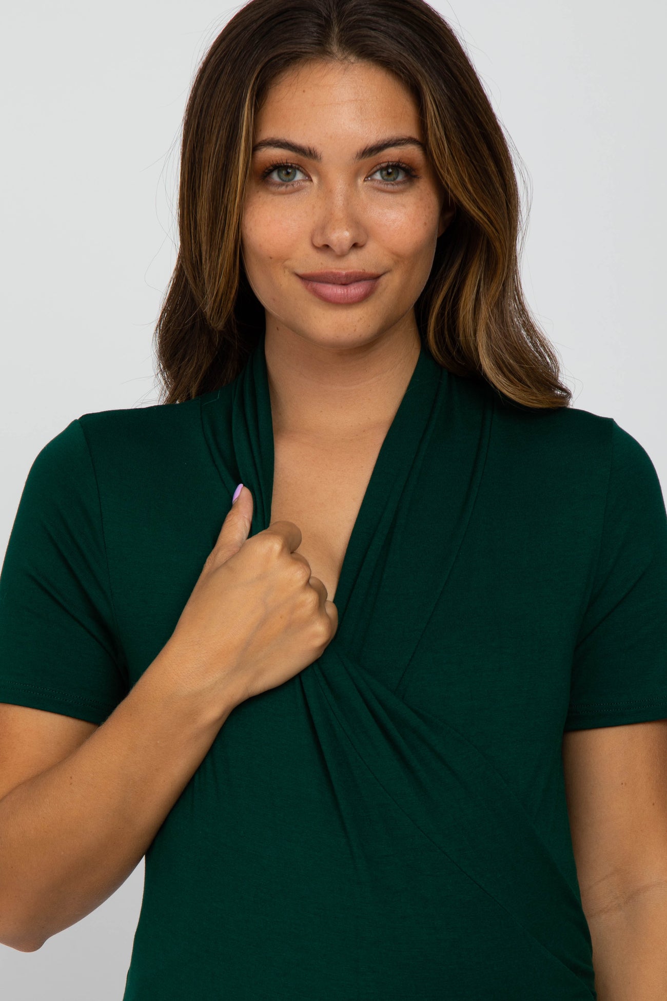 woman wearing a dark green short sleeve maternity top with a wrap design and front ruching, highlighting her baby bump
