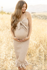 Pregnant woman in a tan gingham dress holding her baby bump in a golden field during a maternity photoshoot