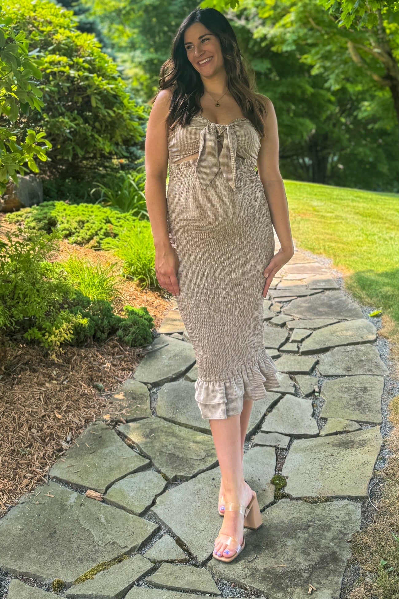 woman wearing a beige maternity dress with a bow detail and ruffle hem, showing her baby bump while walking on a stone path