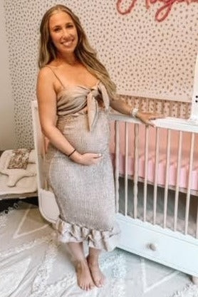 woman wearing a beige maternity dress with a bow tie at the neckline and ruffle hem, showing her baby bump