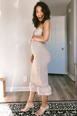 smiling pregnant woman in a beige smocked midi dress and clear heels standing in a room