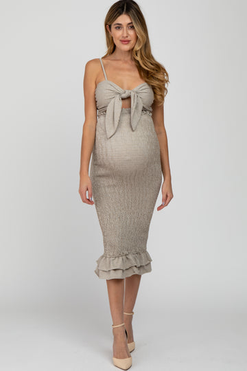 woman wearing a beige maternity dress with a tie front detail and ruffled hem, showcasing her baby bump