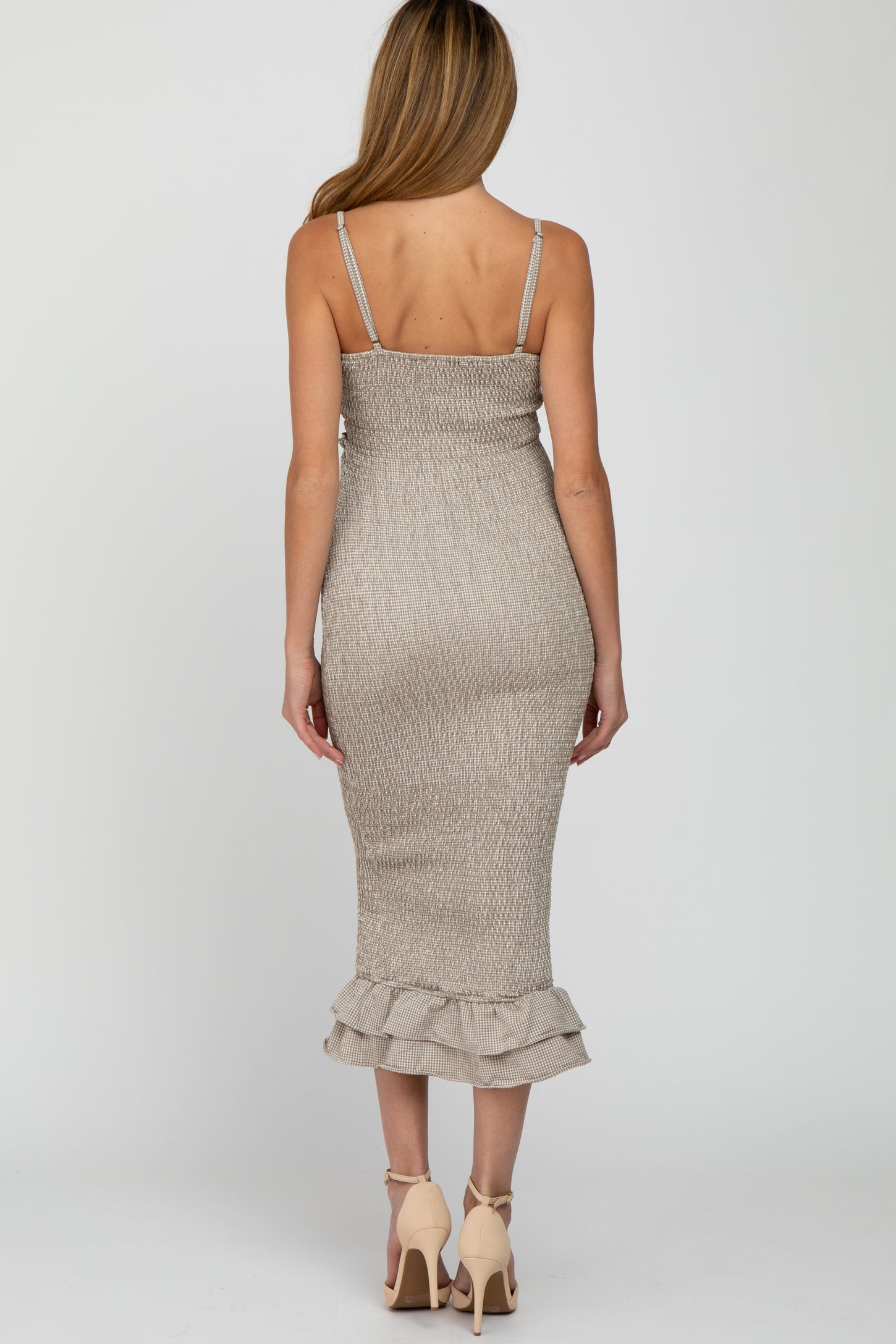 woman wearing a beige maternity dress with adjustable straps and a ruffled hem, showcasing a slight baby bump