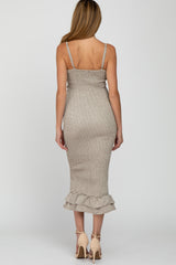 woman wearing a beige maternity dress with adjustable straps and a ruffled hem, showcasing a slight baby bump