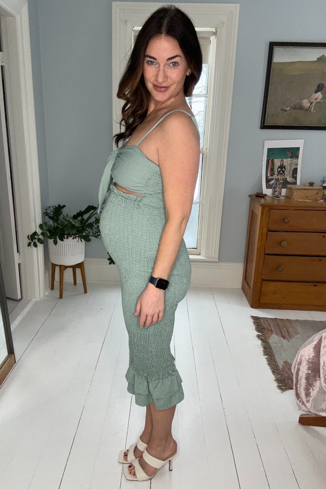 woman wearing a light green maternity dress with a knot front and ruffle hem, showcasing her baby bump