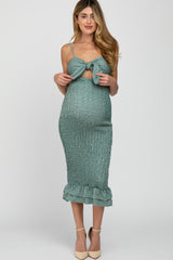 woman wearing a teal maternity dress with a bow detail and ruffled hem, showcasing her baby bump