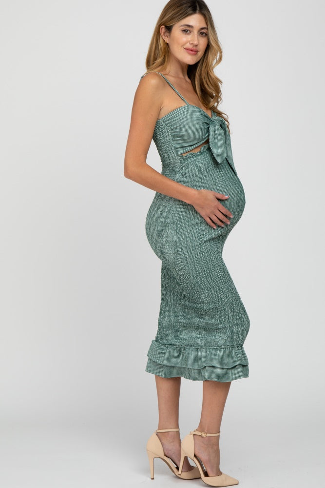 woman wearing a mint green maternity dress with a bow detail and ruffled hem, showing her baby bump.