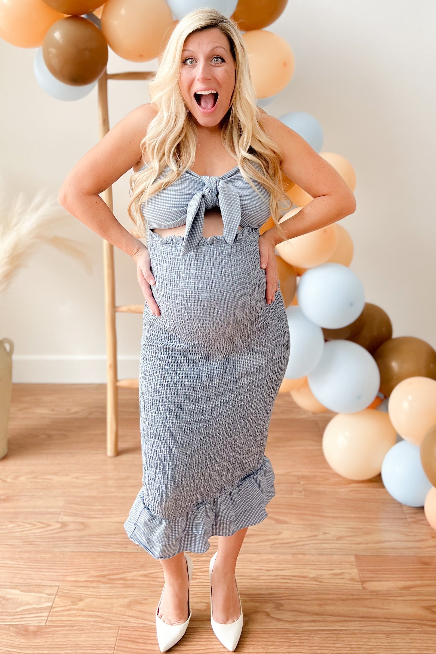 woman wearing a blue and white striped maternity dress with a tie front, showing her baby bump and smiling