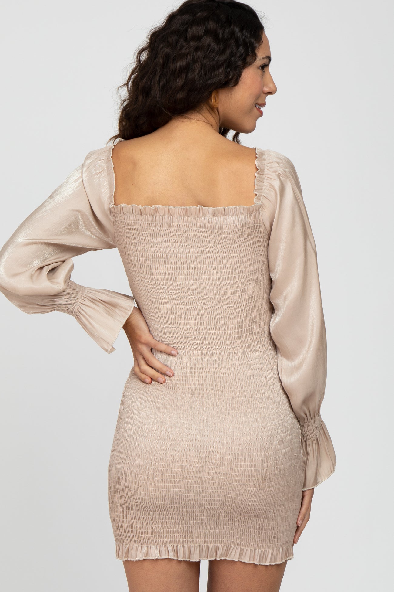 woman wearing a beige smocked mini dress with long satin sleeves and a square neckline, viewed from the back