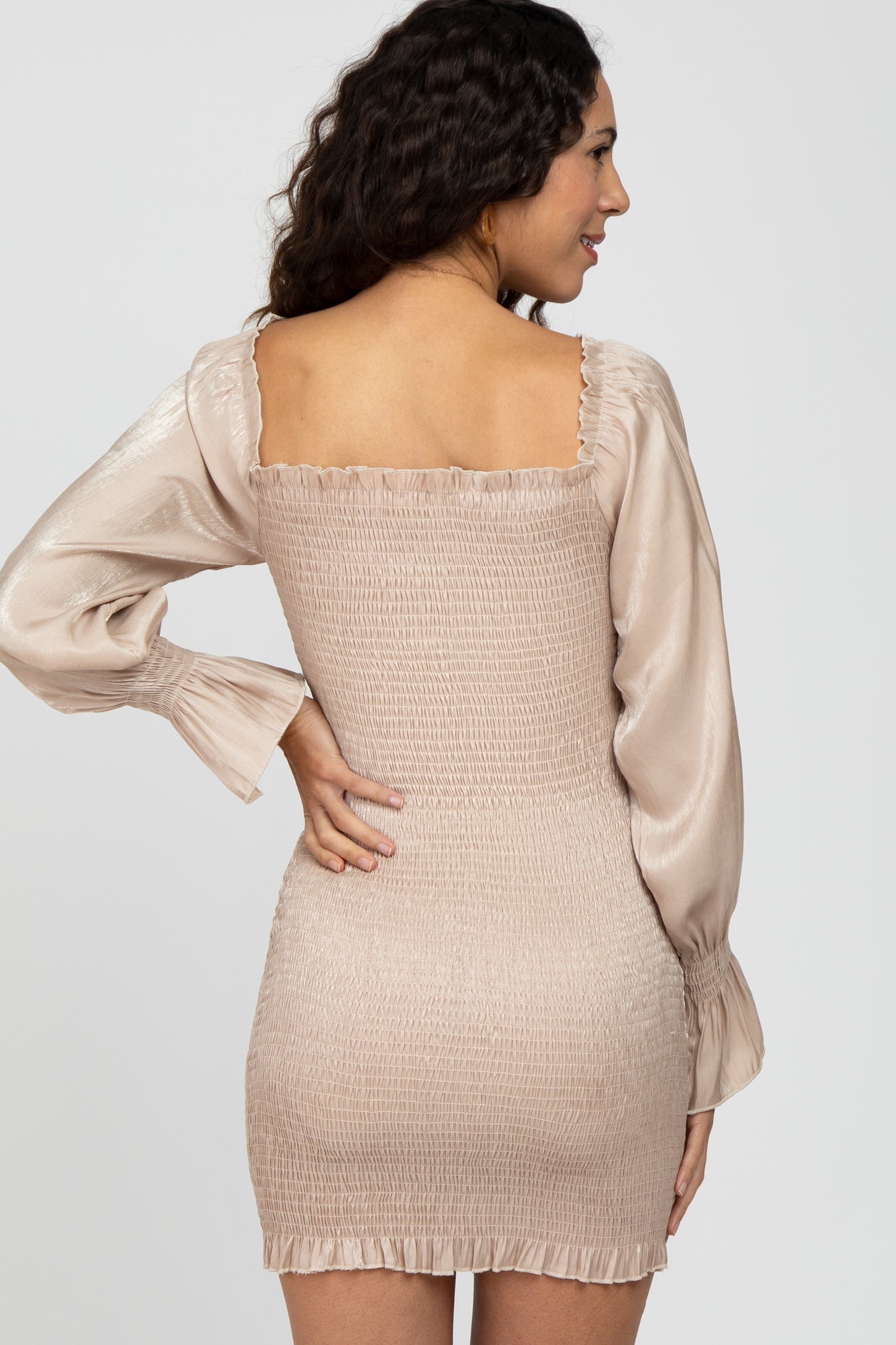 woman wearing a beige smocked mini dress with long satin sleeves and a square neckline, viewed from the back