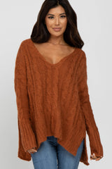 woman wearing an oversized rust cable knit sweater with a deep v-neckline and high-low hem, styled with blue jeans