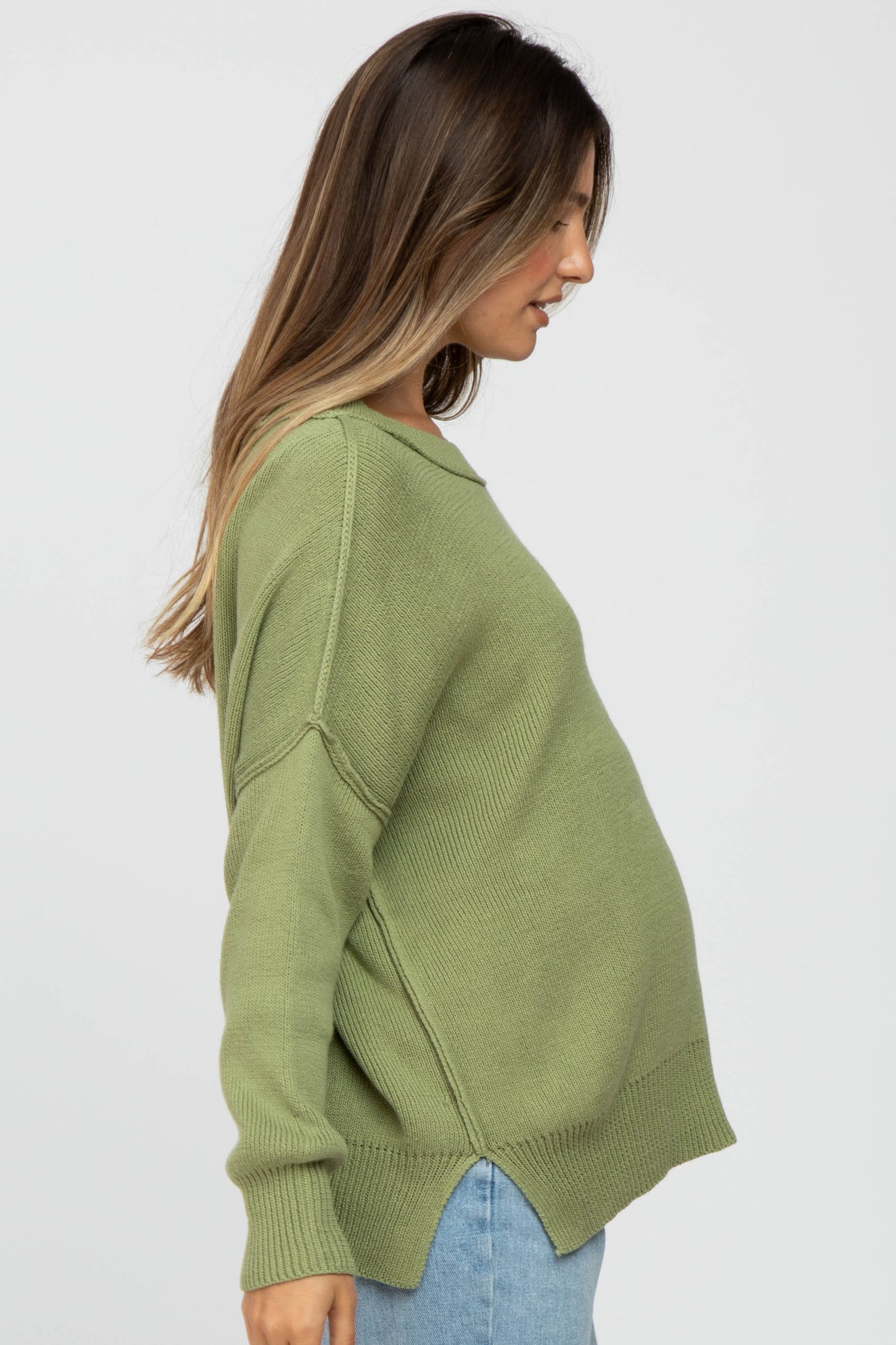 woman wearing a green oversized maternity sweater with a visible baby bump