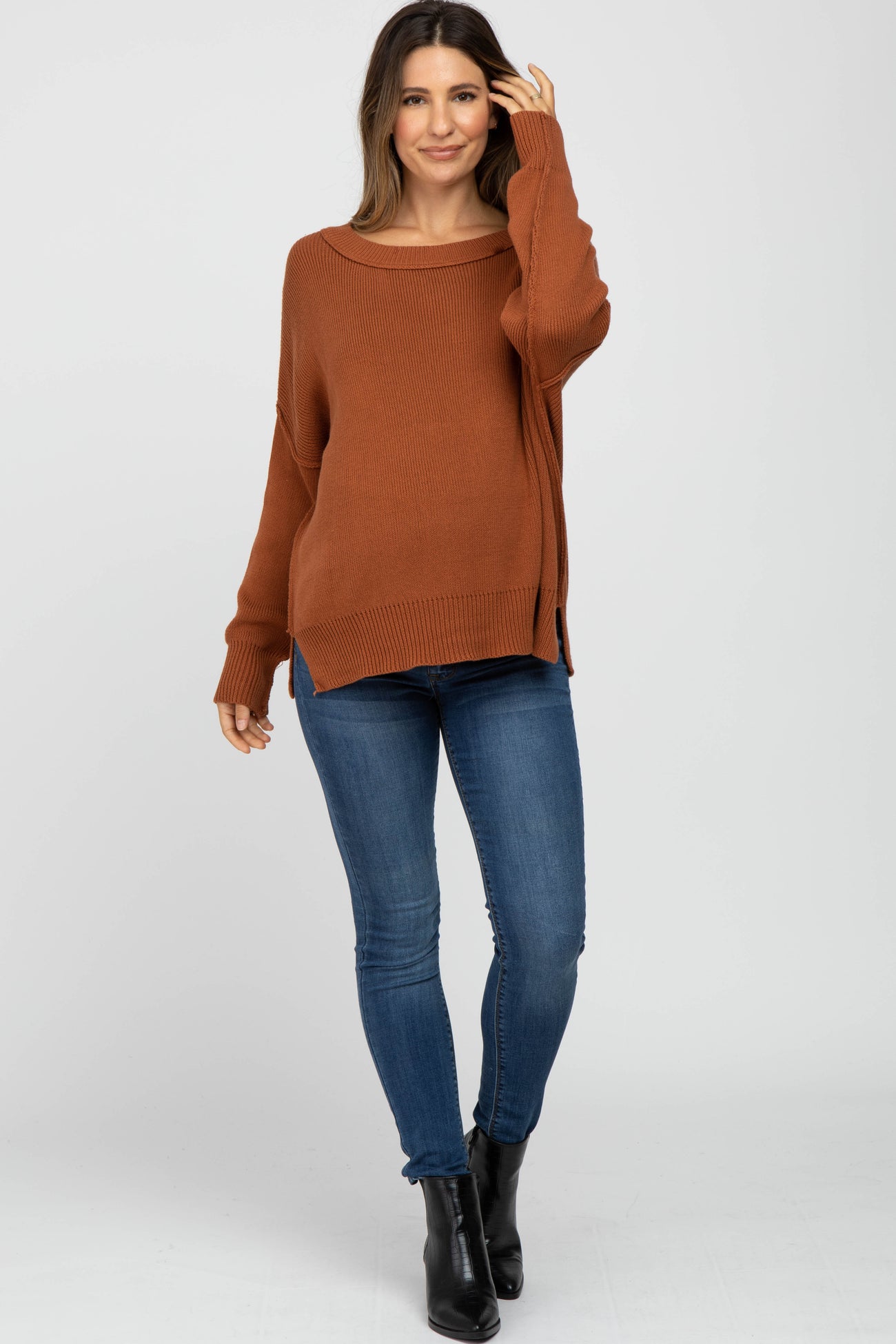 woman wearing a rust-colored oversized ribbed maternity sweater with side slits paired with skinny jeans