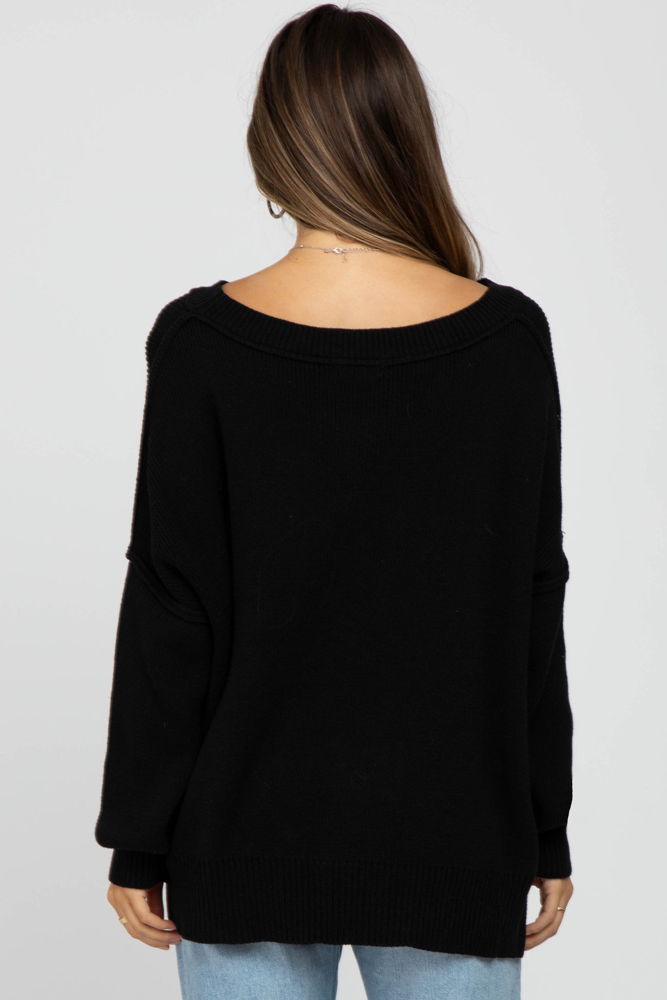 Back view of a woman wearing an oversized black knit sweater with a wide neckline and long sleeves