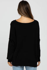Back view of a woman wearing an oversized black knit sweater with a wide neckline and long sleeves