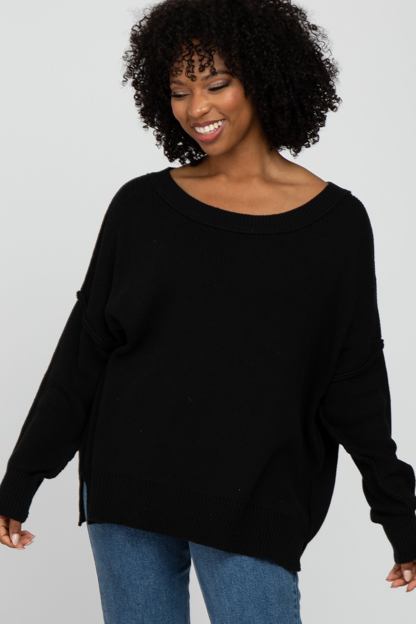 smiling woman with curly hair wearing a black oversized knit sweater and blue jeans
