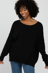 smiling woman with curly hair wearing a black oversized knit sweater and blue jeans