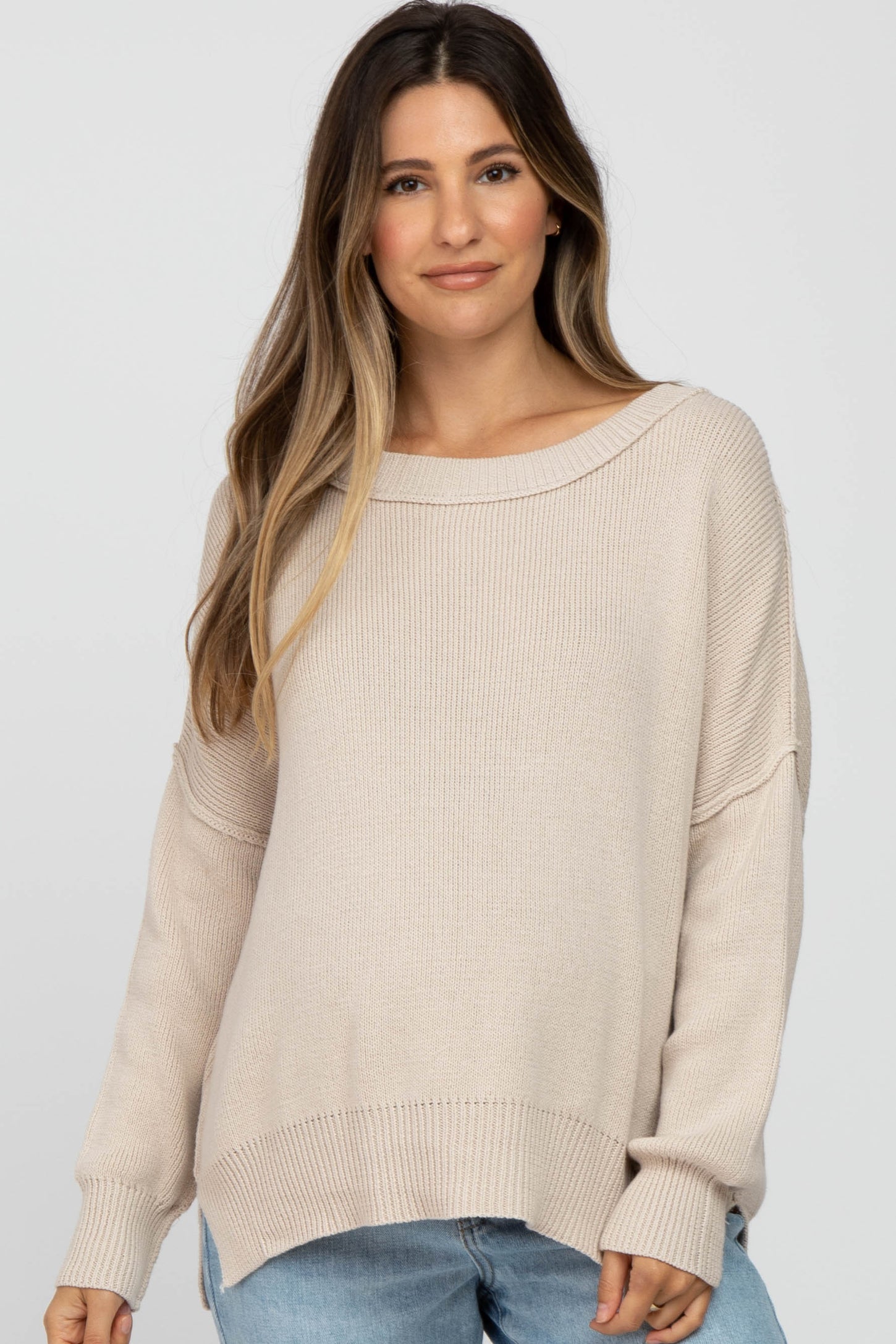 woman wearing a beige oversized knit maternity sweater with a relaxed fit and wide neckline