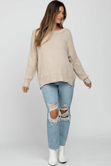 woman wearing a beige oversized maternity sweater and ripped light blue jeans, showing a baby bump