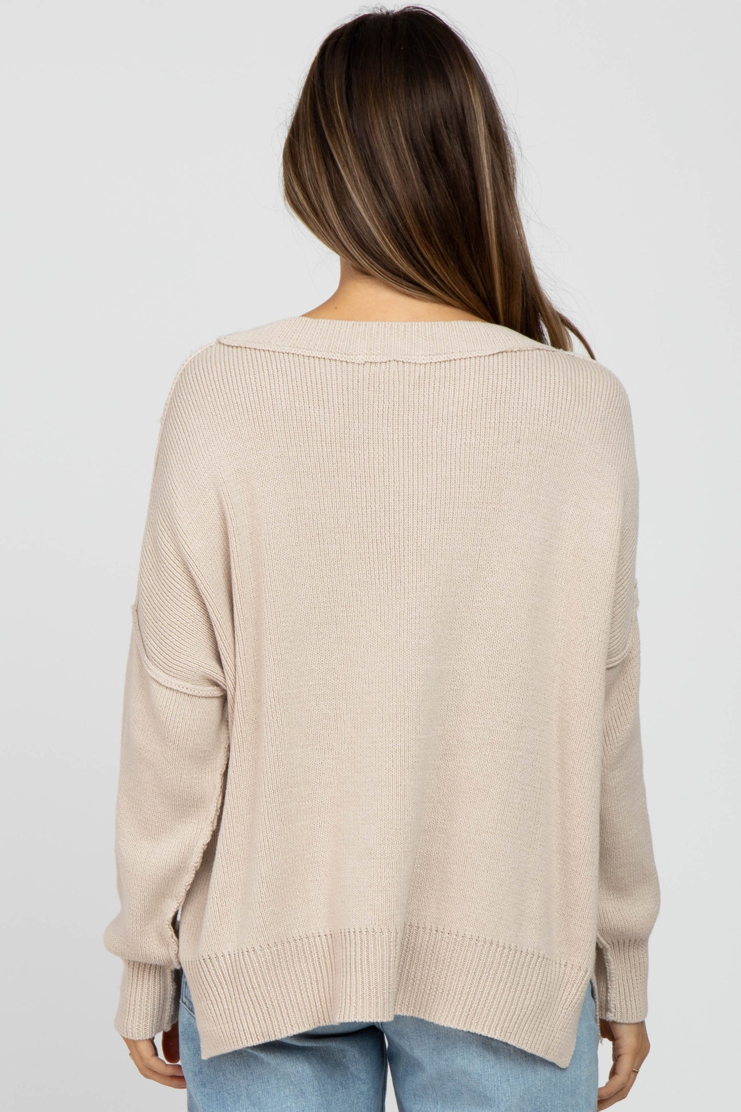 woman wearing a beige oversized maternity sweater, showing the back view with a relaxed fit and dropped shoulder seams