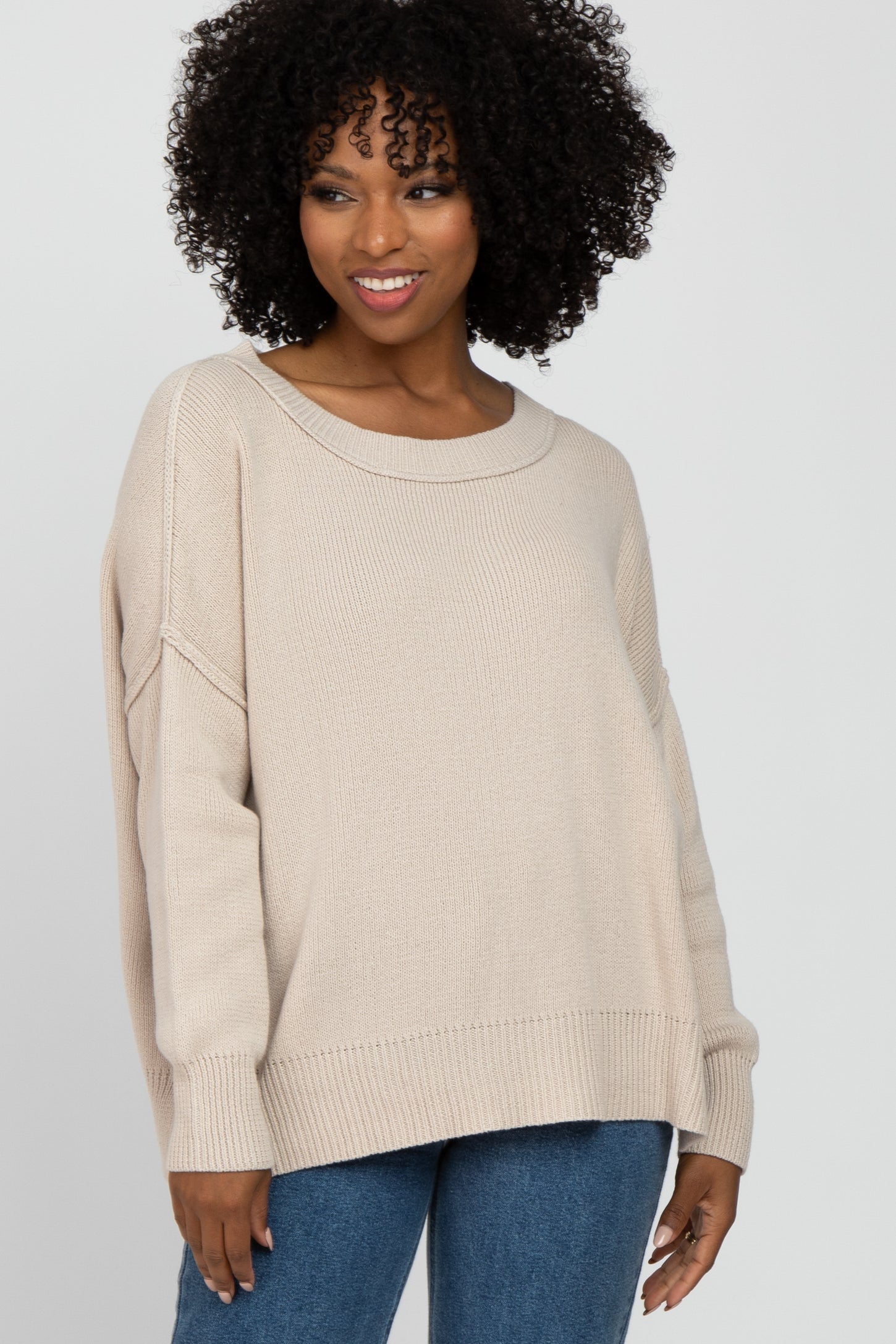 woman wearing a beige oversized sweater with a wide neckline and relaxed fit, paired with blue jeans