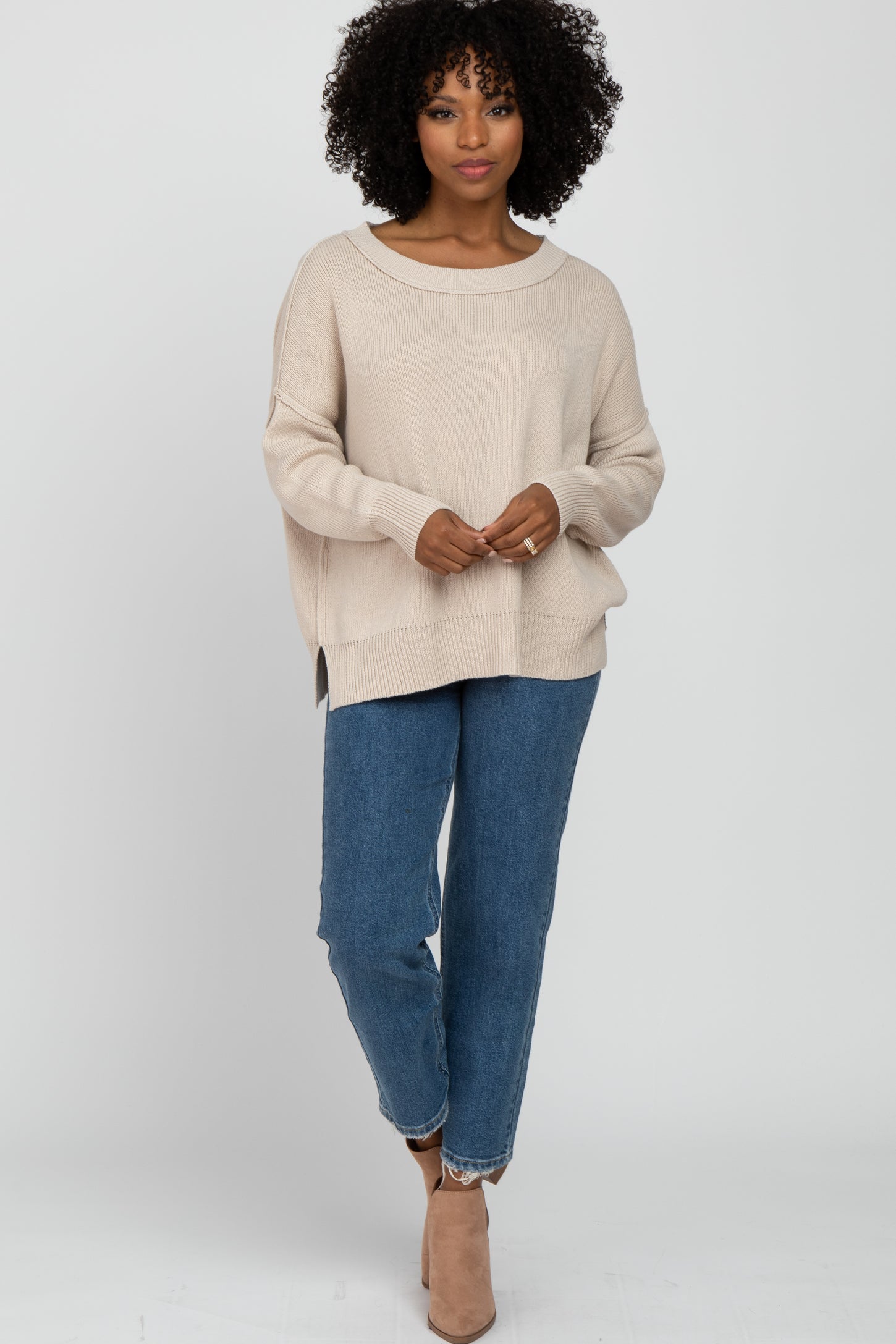 woman wearing a beige oversized knit sweater and blue high-waisted jeans, accessorized with beige ankle boots