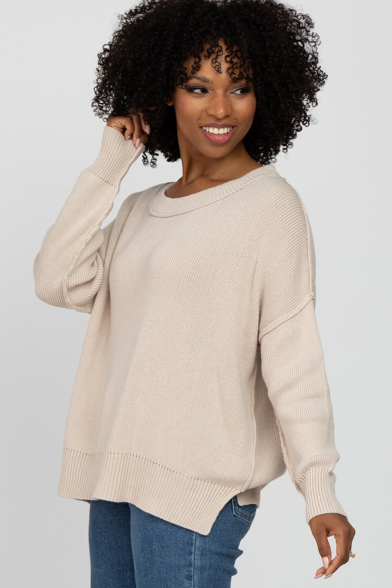 woman wearing a beige oversized knit sweater with ribbed details and a relaxed fit, paired with blue jeans