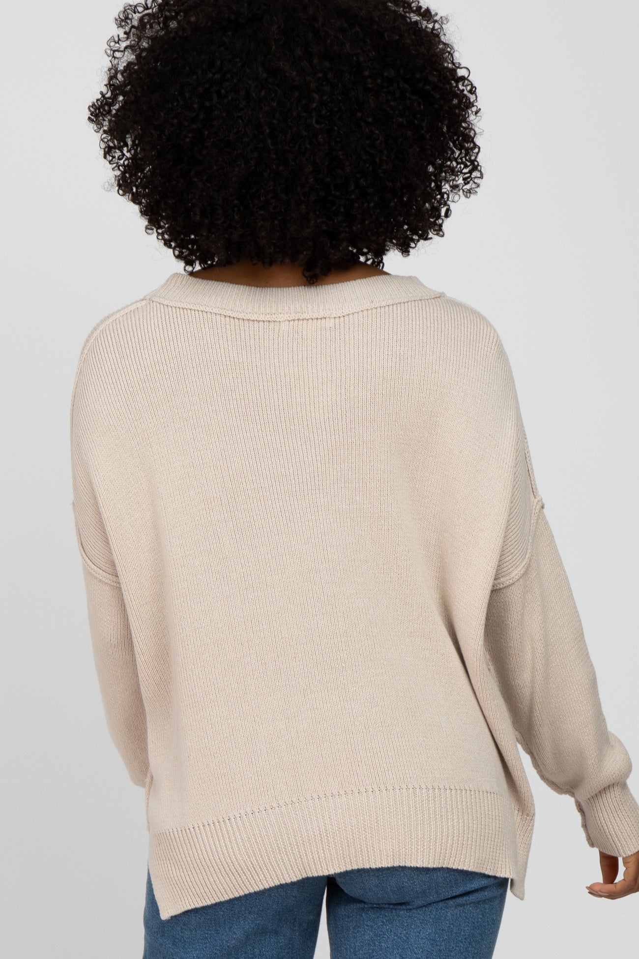 woman wearing a beige oversized sweater with a loose fit and dropped shoulders, viewed from the back