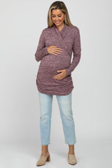 woman wearing a mauve long sleeve maternity top with a wrap design and holding her baby bump