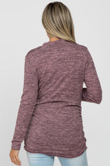 woman wearing a maroon long sleeve maternity top with a relaxed fit and ruched sides, styled with light blue jeans