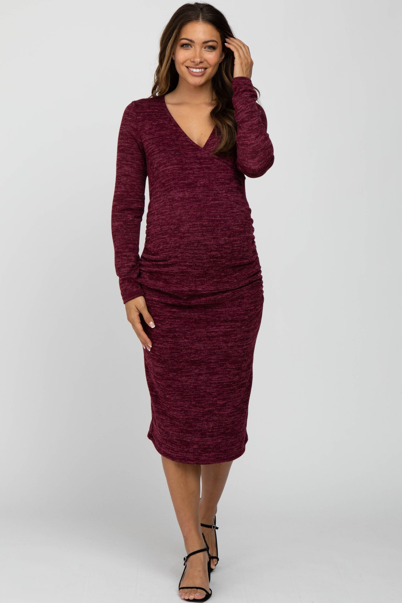 woman wearing a burgundy long sleeve maternity dress with a v-neck and ruched sides, showing her baby bump