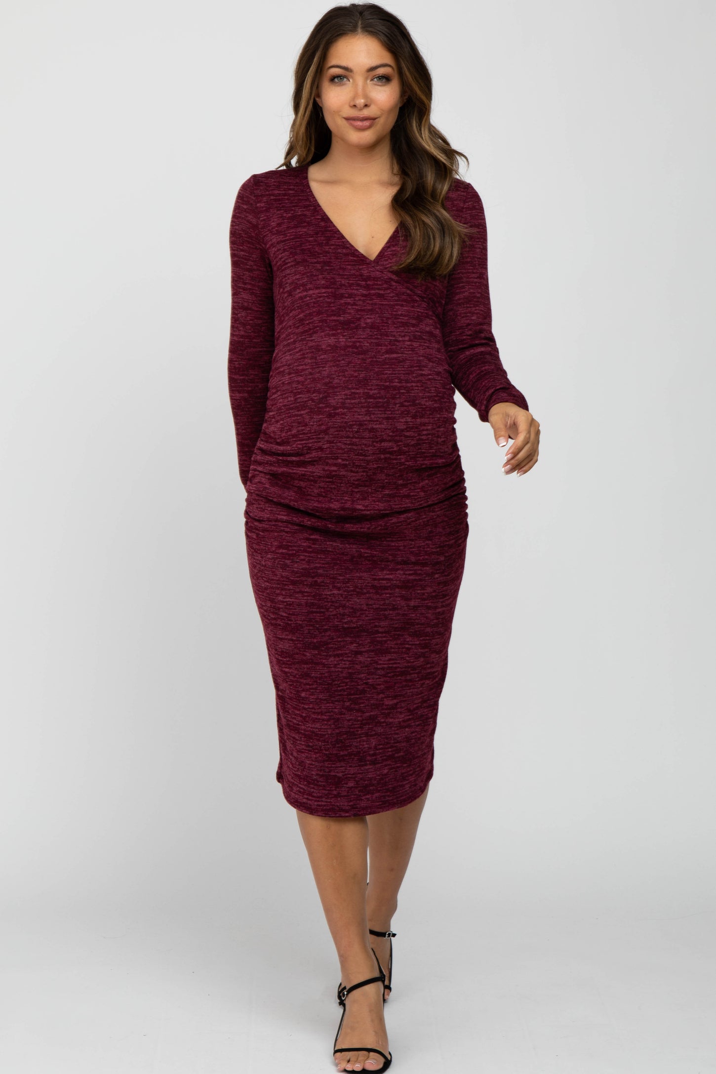 woman wearing a burgundy long sleeve maternity dress with a fitted silhouette and ruching at the sides, showcasing her baby bump