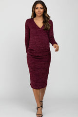 woman wearing a burgundy long sleeve maternity dress with a fitted silhouette and ruching at the sides, showcasing her baby bump