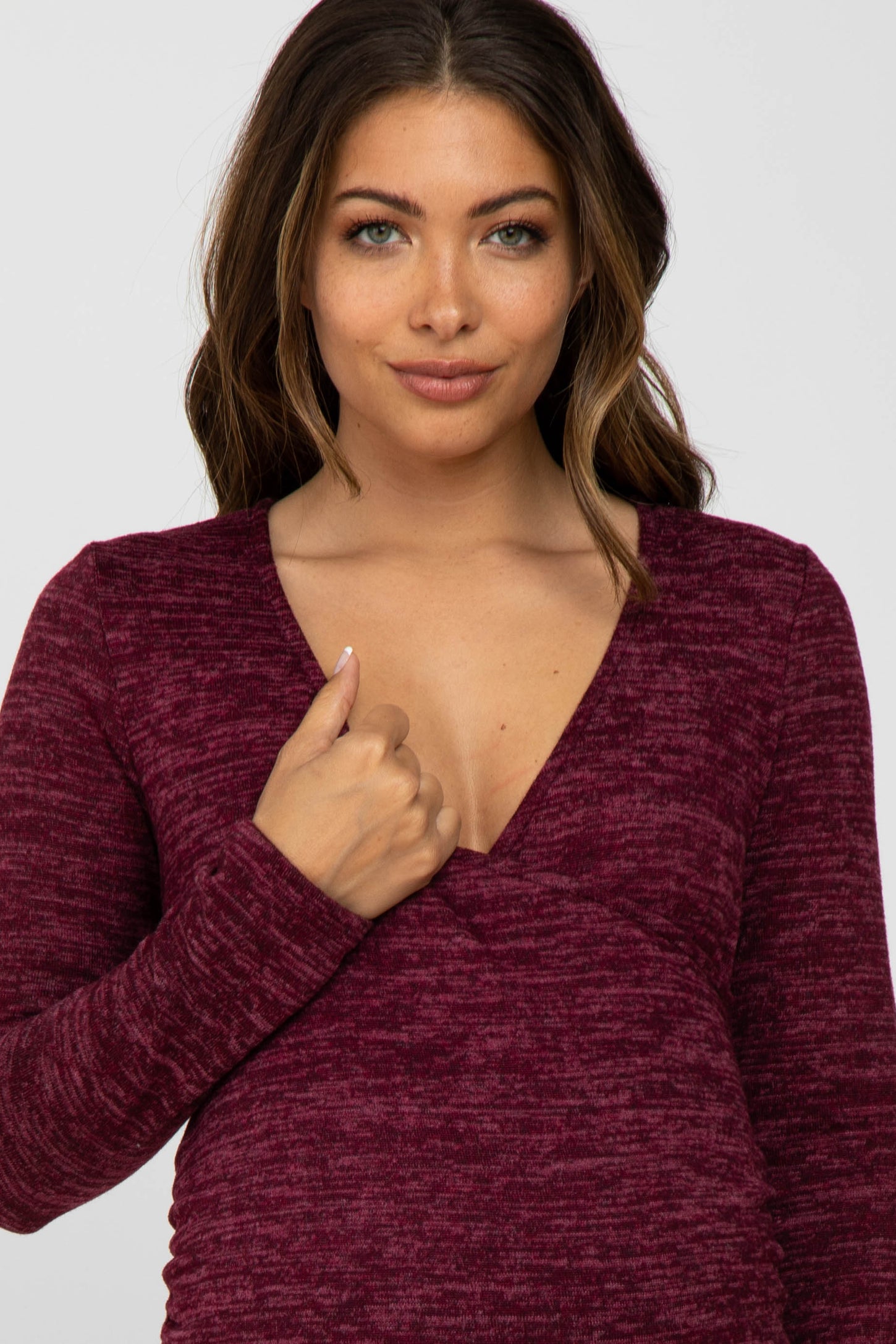 woman wearing a burgundy long sleeve maternity top with a v-neck and thumbhole details, highlighting her baby bump