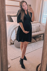 pregnant woman in black velvet maternity dress and ankle boots taking a mirror selfie in a bedroom