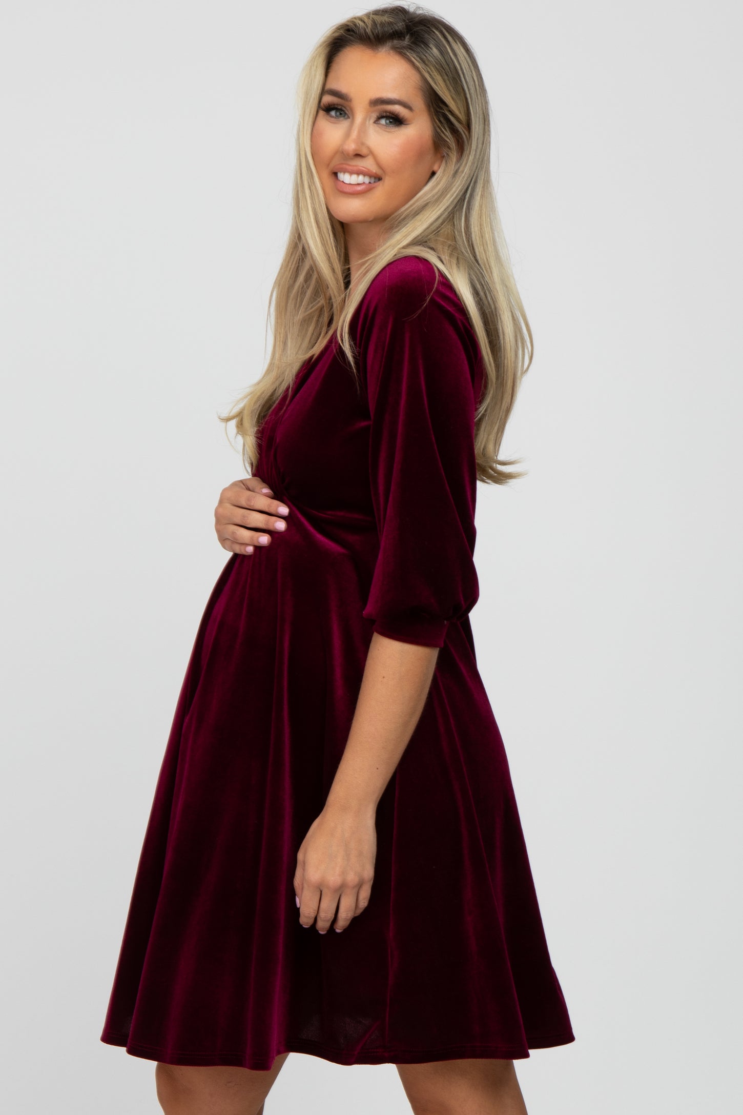 woman wearing a burgundy velvet maternity dress, holding her baby bump with a smile