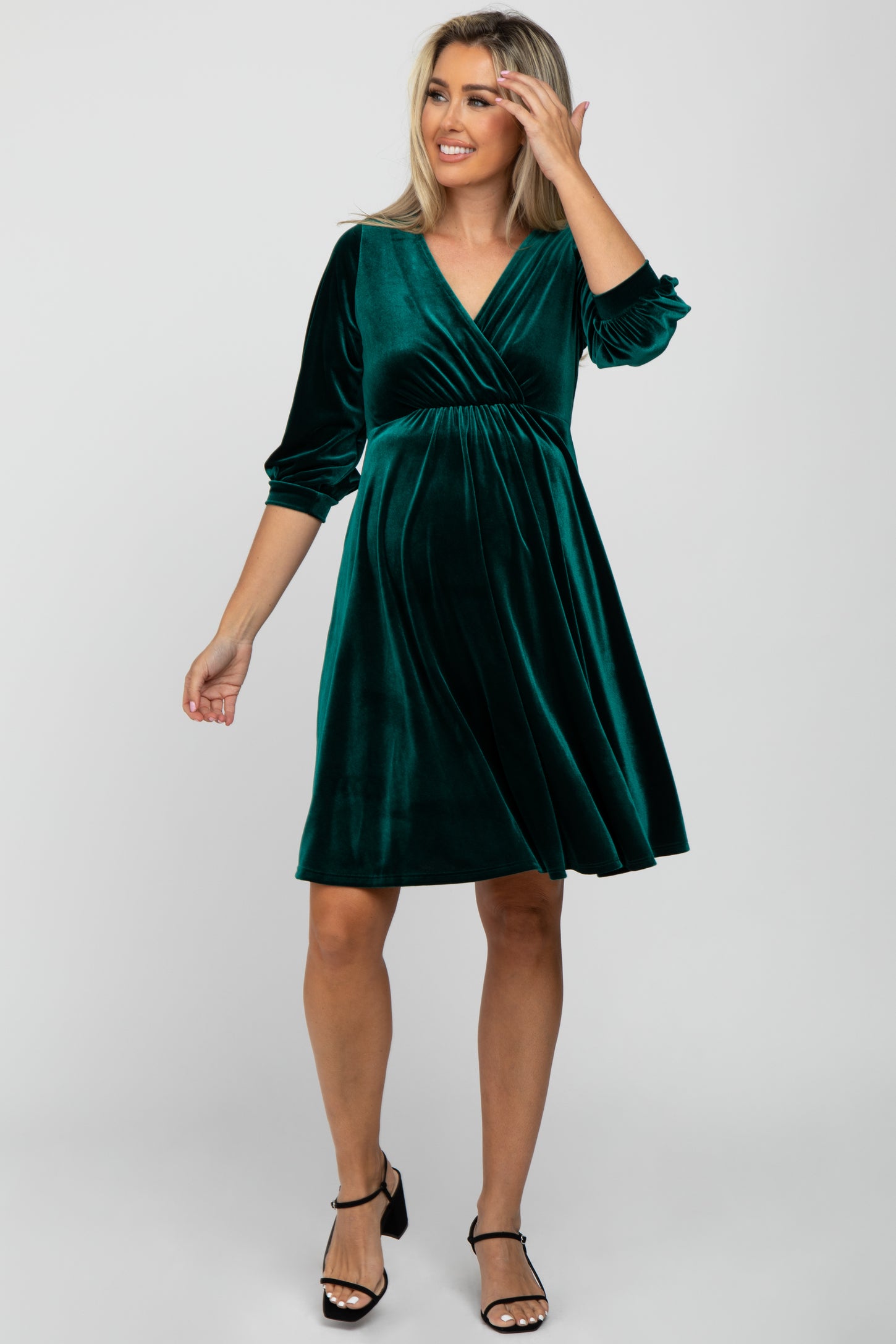woman wearing a green velvet maternity dress with three-quarter sleeves and a v-neck, showing her baby bump