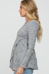 blonde woman wearing a grey long sleeve maternity top with a draped front and blue jeans
