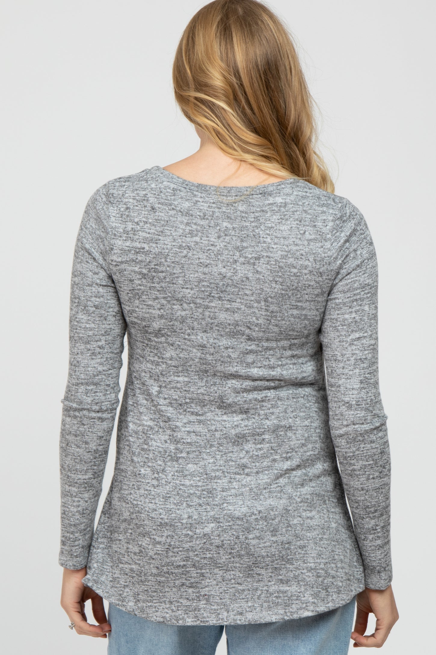 woman wearing a heather gray long sleeve maternity top with a rounded hem and a relaxed fit from the back view