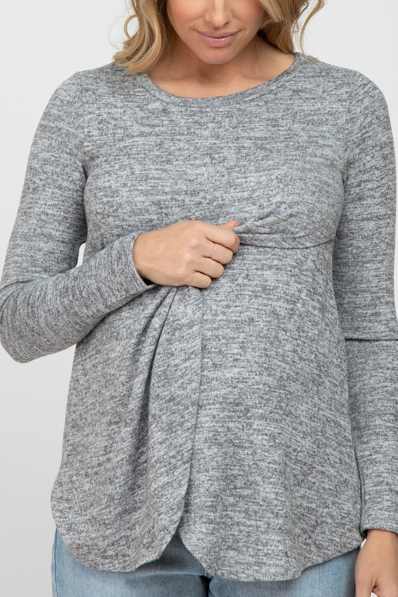woman wearing a gray long sleeve maternity top with a knotted front detail and holding her baby bump.