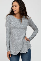 woman wearing a gray long sleeve top with a curved hem and textured fabric, paired with blue jeans