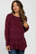 woman wearing a burgundy long sleeve maternity top with a scoop neckline and side slits, styled with jeans