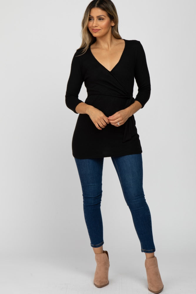 woman wearing a black wrap top with three-quarter sleeves and blue skinny jeans, standing in a casual pose